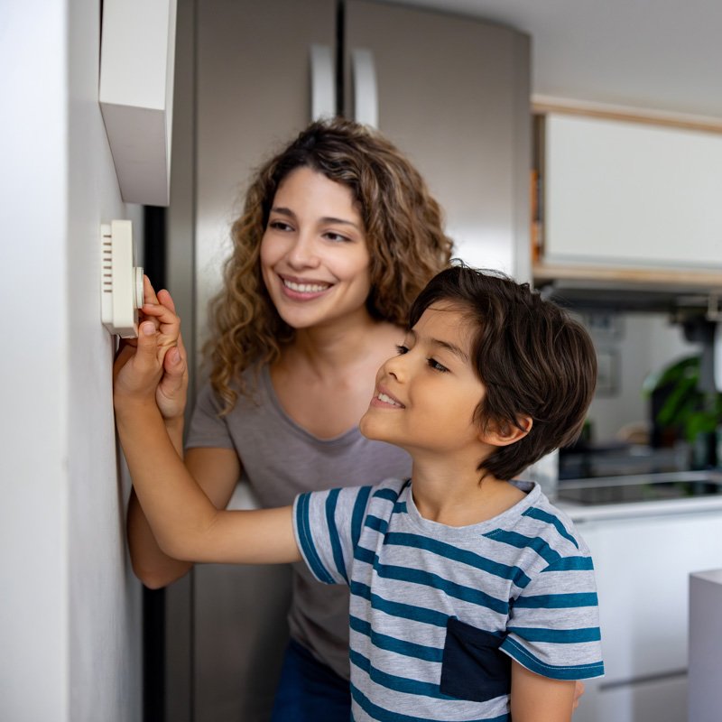 An adult and a child adjust a wall thermostat in a modern kitchen in Seattle, WA