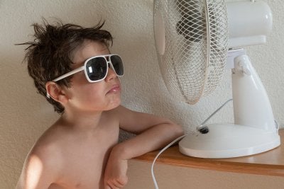 Boy enjoys the cool air from a table fan while reading to buy the right air conditioner in Seattle.